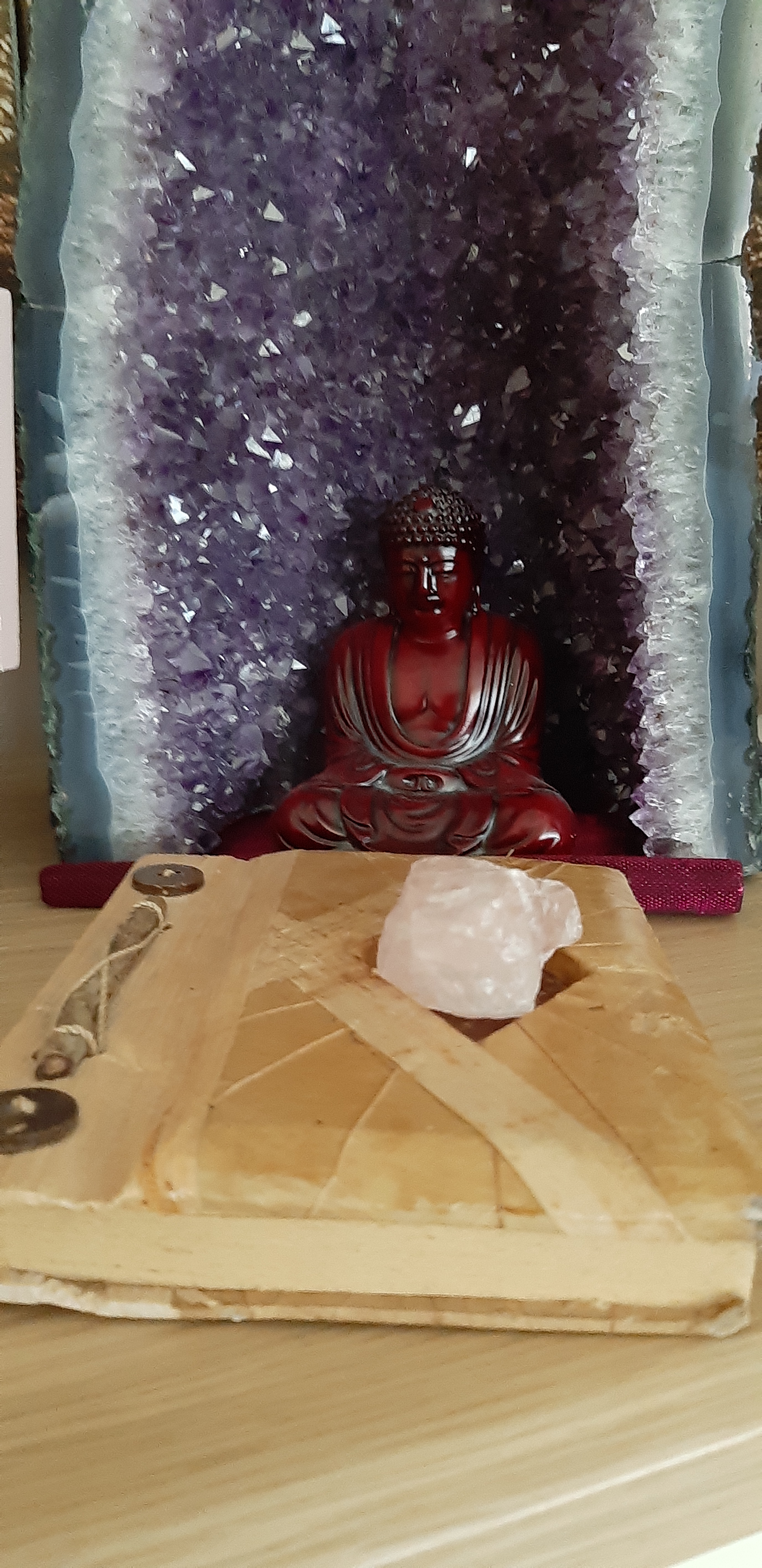 Buddha statue in front of an amethyst crystal geode with a journal and rose quartz crystal in the foreground